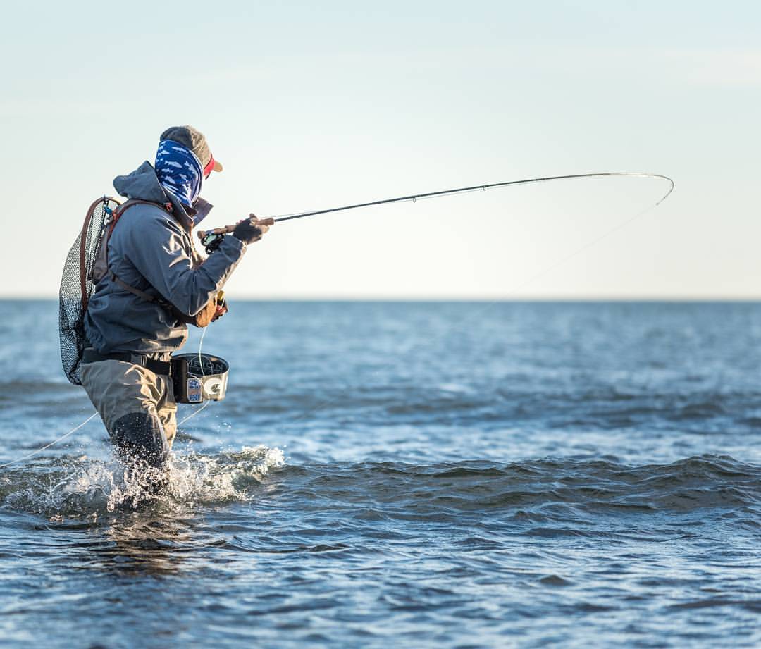 En sportfiskare i fiskeutrustning kastar med sitt spö i havet under en fiskeresa. Klart väder och lugna vågor.