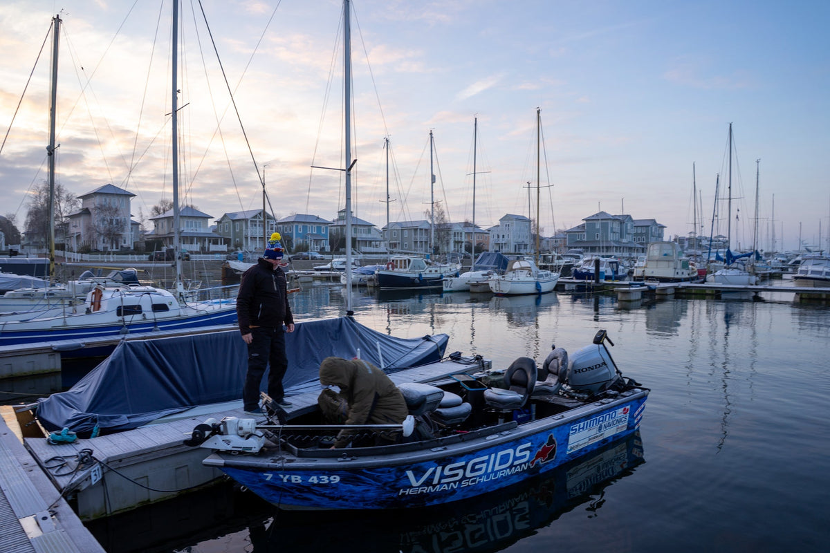 Två sportfiskare står på en liten blå fiskebåt vid bryggan bland segelbåtar i Nederländerna