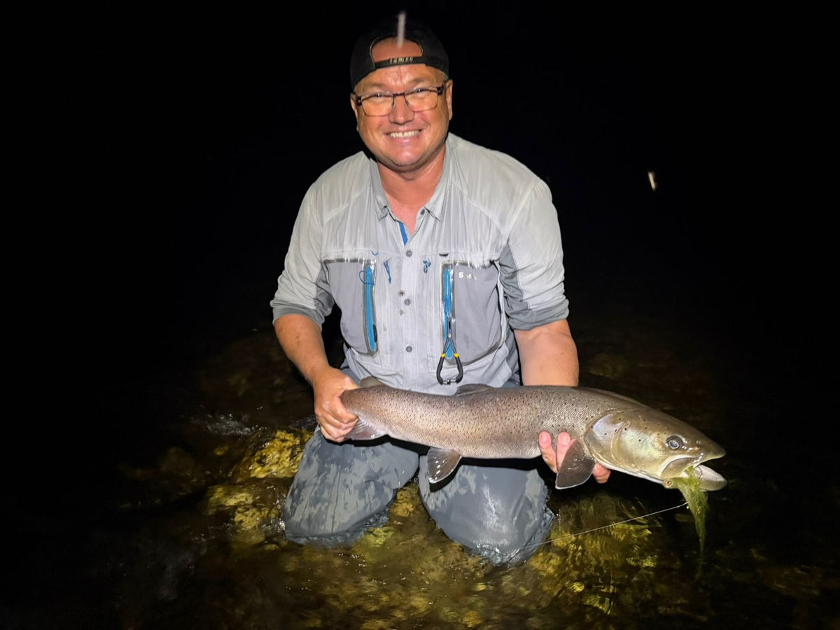 Flugfiskare knäböjer i älven med en hucho hucho (donaulax) fångad på streamer i mörkret i Montenegro