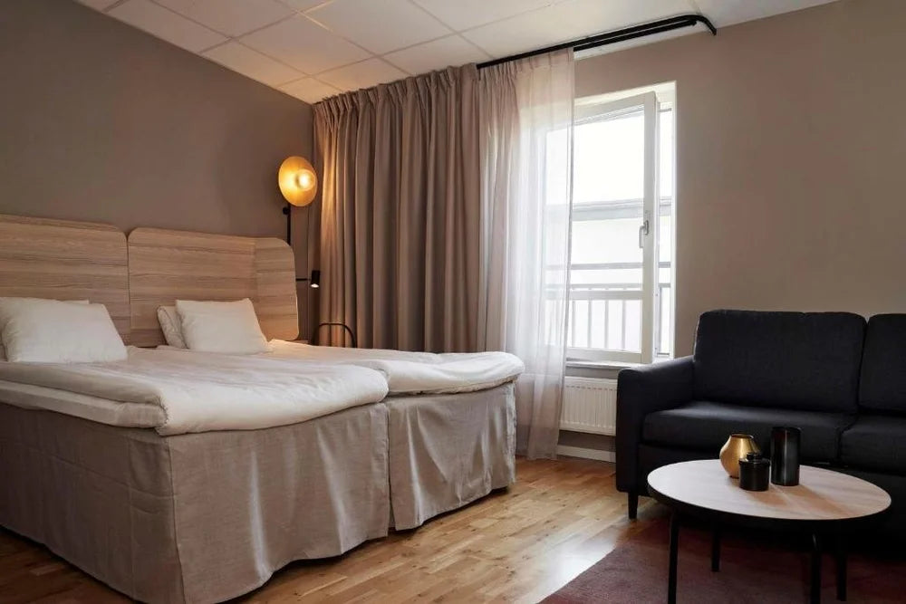 Modernt hotellrum med två sängar, soffa, soffbord och stora fönster-perfekt avslappning efter sportfiskeäventyr.