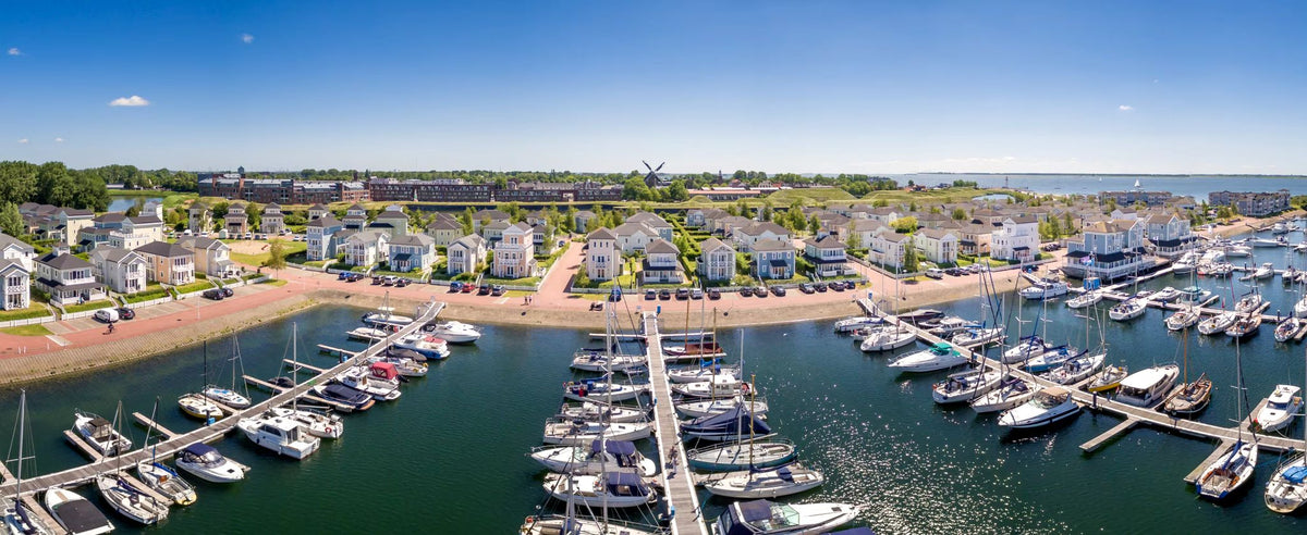 Flygfoto över marina med båtar och yachter, perfekt för fiskeresa. Moderna hus vid stranden, träd och en väderkvarn bakom.