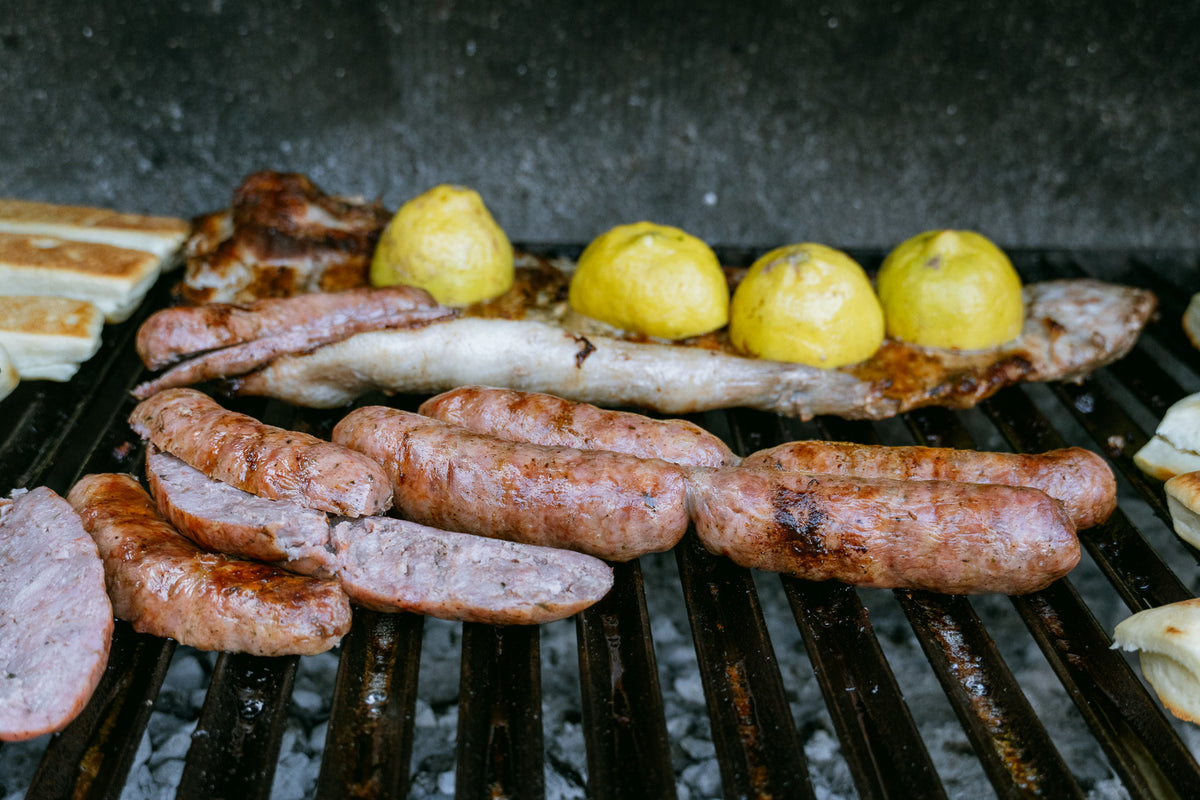 Grill med korvar, köttbitar och halverade citroner över glödande kol - perfekt måltid efter en lyckad fiskeresa.