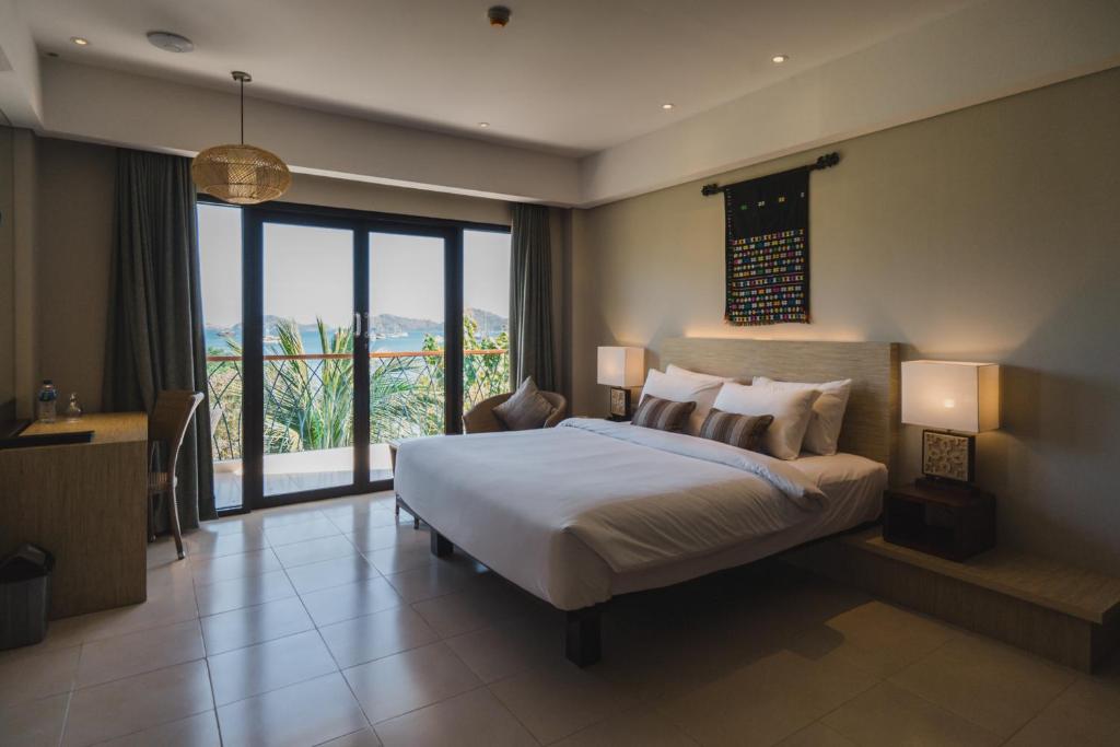 Ett modernt hotellrum med en stor säng, två lampor, ett skrivbord och glasdörrar ut till en balkong med utsikt över havet och kullarna – perfekt för avkoppling efter en dag på fisketur.