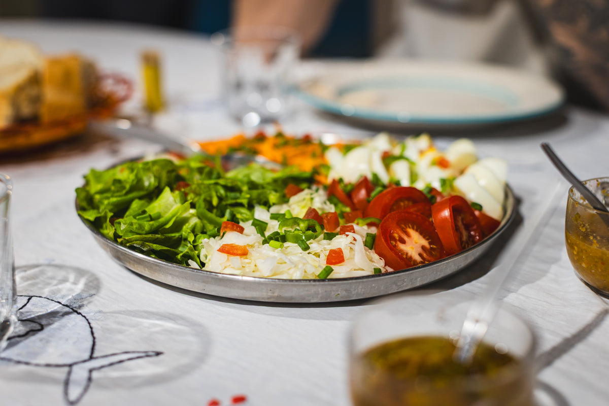 Metalltallrik med sallad, ägg och grönsaker, idealisk för sportfiskare på fiskeresa. Drycker och tillbehör runt tallriken.