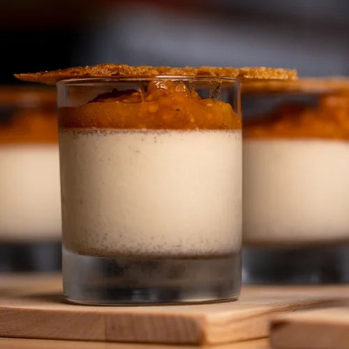 Närbild på dessert i glas med vit bas, apelsinkompott och krispigt täcke - perfekt efter fiskeresa, på träbord.