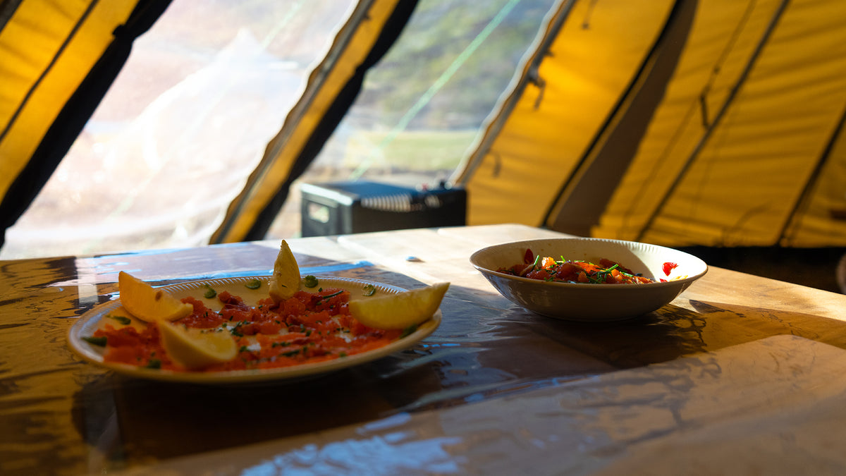 Två tallrikar med mat, laxskivor och citronklyftor samt sallad på ett bord i ett soligt tält efter en lyckad fiskeresa.