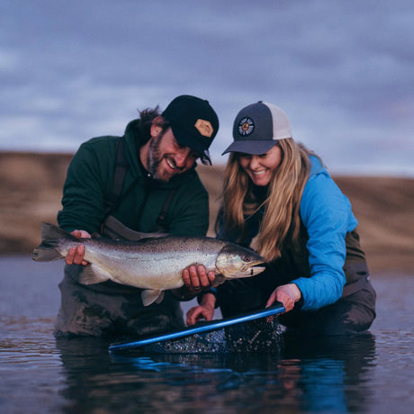 Två sportfiskare håller upp en stor fisk vid Rio Menendez, Argentina, under en fiskeresa i vackert natur- och vattenlandskap.