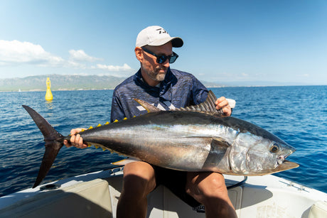 Fiskare beundrar en blåfenad tonfisk i båten med en gul boj och kustbergen i bakgrunden